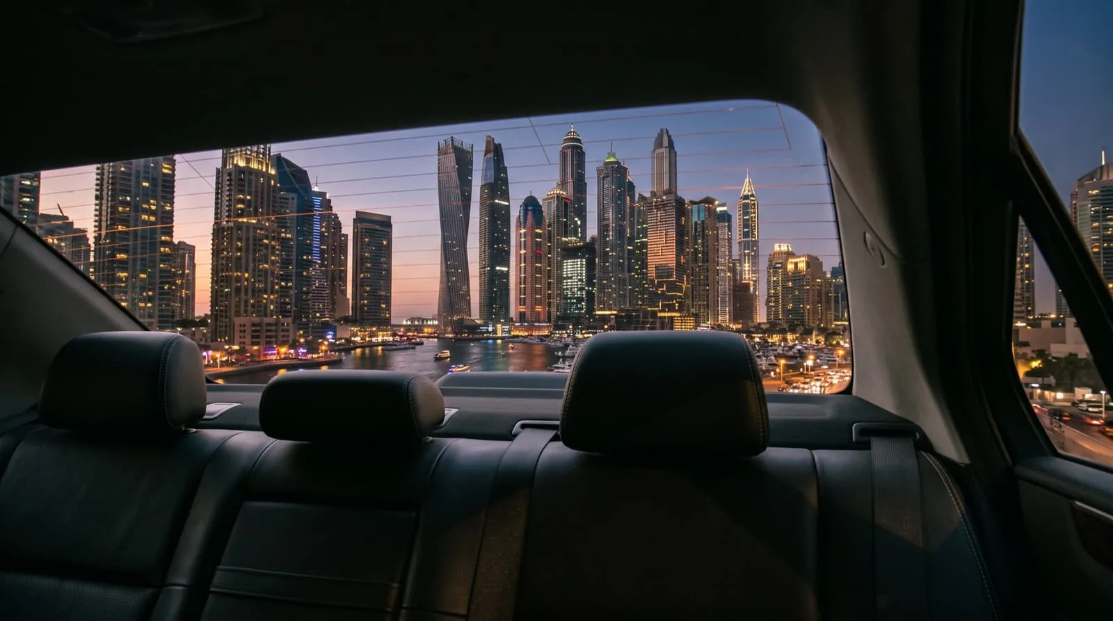 The Dubai Marina skyline at dusk, seen from the rear seat of an executive sedan